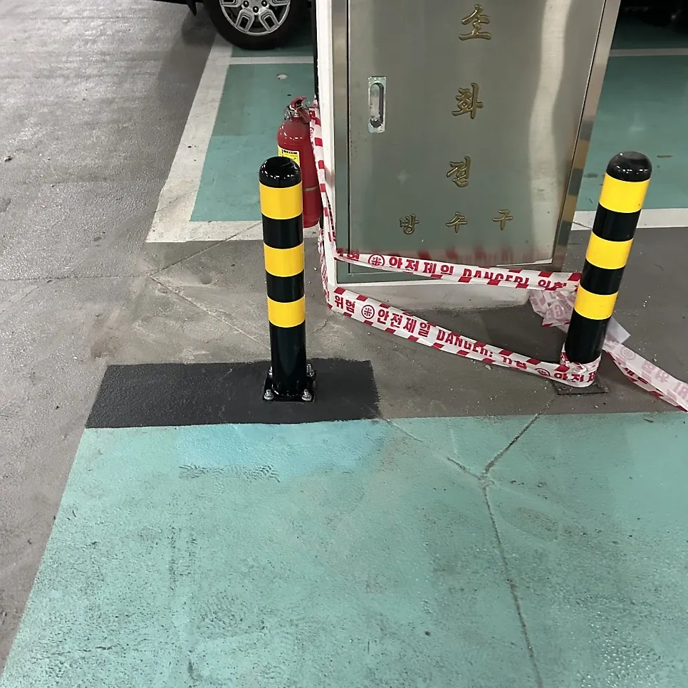 청록색 바닥 소화전함 앞 노랑·검정 볼라드